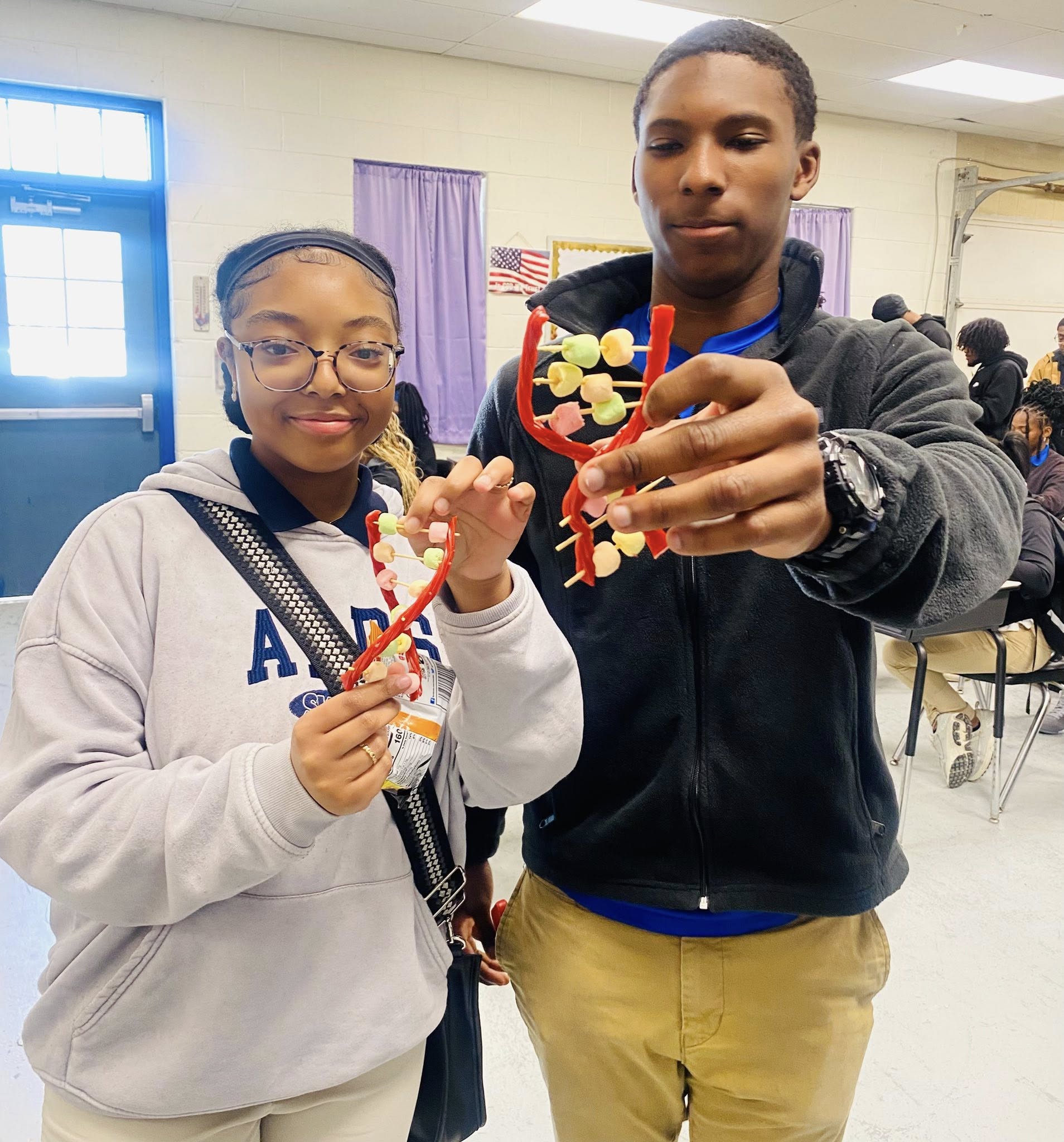 A girl and a boy holding miniature DNA strands made of Twizzlers, toothpicks, and mini marshmallows.